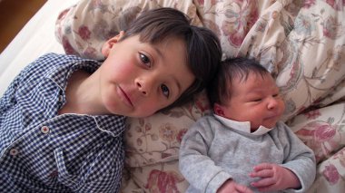 Çiçekli bir yatakta yenidoğan kardeşinin yanında yatan küçük çocuk, ömür boyu sürecek bir bağın başlangıcını ve bir yuva ortamındaki kardeşler arasındaki erken bağlantıyı resmediyor.