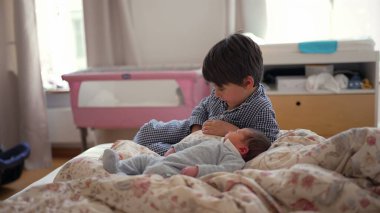 Ağabeyim, yeni doğan kardeşinin yanında, yatakta oturuyor, onları düşünceli bir ifadeyle gözlemliyor, kardeş ilişkisinin ilk aşamalarında sakin ve içsel bir anı yakalıyor.