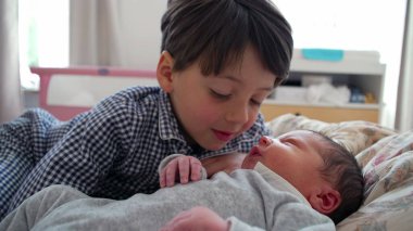 Ağabeyi, yeni doğan kardeşiyle yatakta etkileşim halinde. Sıcak, aile odaklı bir evde kardeşler arasındaki özel bağ ve ilgiyi vurguluyor.