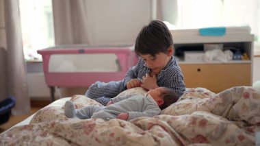 Ağabeyim, yeni doğan kardeşinin yanında, yatakta oturuyor, onları düşünceli bir ifadeyle gözlemliyor, kardeş ilişkisinin ilk aşamalarında sakin ve içsel bir anı yakalıyor.