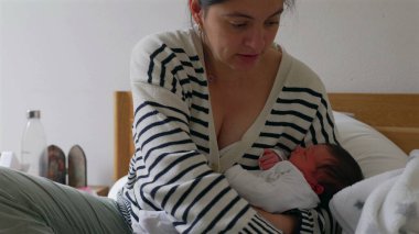 Anne yeni doğmuş bebeğini yatağına yatırıyor, hem rahat hem de sakin bir şekilde. Huzurlu bir yuvada anne ve çocuğu arasında paylaşılan samimi bağları ve şefkatli sevgiyi gösteriyor.