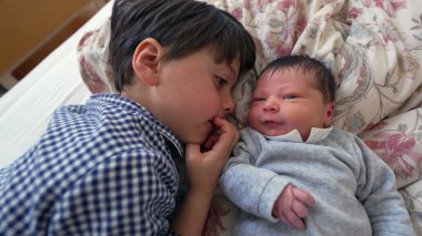 Ağabeyi, yeni doğan kardeşiyle yan yana yatar ve iki kardeş arasındaki sevgi ve sevgiyi vurgulayan yakın ve samimi bir yakınlaşma anını paylaşır.