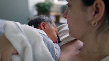 Yeni doğmuş bebeğini nazikçe göğsüne yakın tutan bir annenin yan görüntüsü, anne ve çocuk arasında paylaşılan derin bağları, sıcaklığı ve güvenliği yakalayarak besleyici bir çevrede paylaşıyor.
