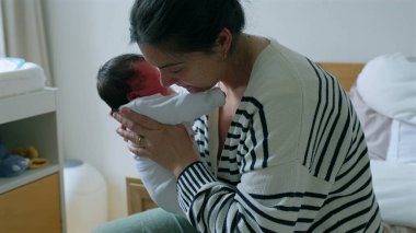 Anne, yeni doğmuş bebeğini kucağında tutuyor ve rahatlatıyor. Her ikisi de sevgi ve bağla dolu hassas bir anı paylaşıyor. Anne ve çocuk arasındaki samimiyet, ilgi ve bağın altını çiziyor.