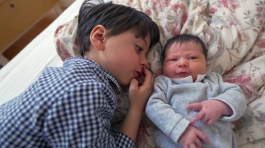 Ağabeyi, yeni doğan kardeşiyle yan yana yatar ve iki kardeş arasındaki sevgi ve sevgiyi vurgulayan yakın ve samimi bir yakınlaşma anını paylaşır.