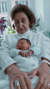 Büyükannesi uyuyan yeni doğan torununu kucaklıyor, huzurlu ve rahatlatıcı bir dinlenme anı yakalıyor ve sakin bir ev ortamında iletişim kuruyor.