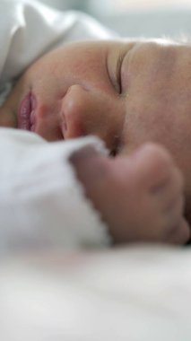 Yeni doğmuş bir bebeğin huzur içinde uyuduğu yakın plan, odak noktasında narin yüz hatları, yumuşak battaniyeler, sıcak ve rahatlatıcı atmosfer ile çevrili huzurlu ve sessiz bir dinlenme anı yakalıyor.
