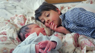 Büyük kardeş yeni doğan kardeşe merak ve sevgiyle bakıyor. Sıcak ve şefkatli bir evde derin bir bağ ve bağ kurma anı yaratıyor.