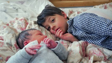Büyük kardeş yeni doğan kardeşe merak ve sevgiyle bakıyor. Sıcak ve şefkatli bir evde derin bir bağ ve bağ kurma anı yaratıyor.