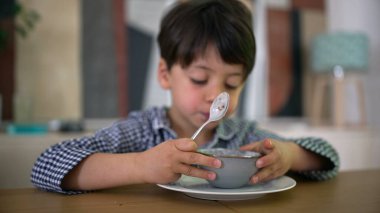 Çocuk kameraya boş bir kase gösteriyor, yemeğinin sonunu simgeliyor, yemek masasında neşeli ve etkileşimli bir an yakalıyor.