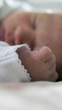 Yeni doğmuş bir bebeğin huzur içinde uyuduğu yakın plan, odak noktasında narin yüz hatları, yumuşak battaniyeler, sıcak ve rahatlatıcı atmosfer ile çevrili huzurlu ve sessiz bir dinlenme anı yakalıyor.