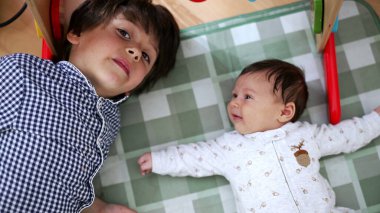 Ağabeyi bir oyun hasırında kardeşinin yanında yatıyor, karşılıklı gülüşmeler ve sevgi dolu bakışlar atıyor, kardeşlik ve sevgi dolu bir anı vurguluyor.