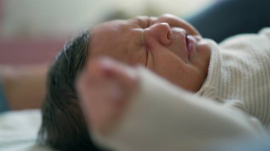 Uzamış koluyla hapşıran bir bebeğin yakın çekimi, ani hareketi gösteriyor. Bebek sıcak bir ev ortamında bir yatakta yatıyor.