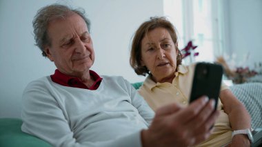 Üst düzey çiftlerin akıllı bir telefona sarılıp baktıkları, aile üyeleriyle video görüşmesi yaptıkları, elleri ve yüzleri hafifçe bulanıklaştığı, iletişim ve teknoloji kullanımını paylaştığı,