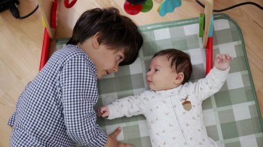 Ağabeyi yerde, küçük kardeşinin yanında yatıyor. Göz teması ve bağlantı kurduğu hassas bir anı, kardeş bağı ve aile sevgisini neşeli bir ortamda paylaşıyor.