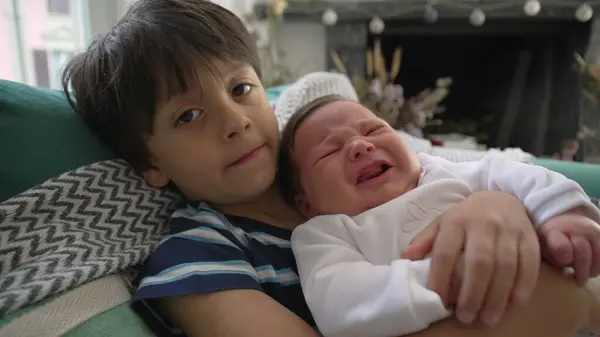 stock image Older brother tenderly holding and comforting crying newborn sibling on the couch, creating a heartwarming family moment