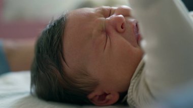 Uzamış koluyla hapşıran bir bebeğin yakın çekimi, ani hareketi gösteriyor. Bebek sıcak bir ev ortamında bir yatakta yatıyor.