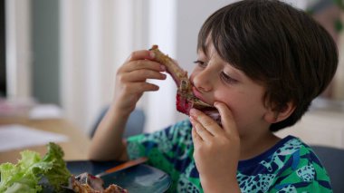 Çocuk kararlı bir bakışla kaburga çiğniyor, yeme eylemiyle meşgul. Etli bir atıştırmalığın keyfini çıkardığım eğlenceli bir an.