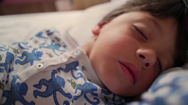 Yan yana uyuyan çocuğun yakın çekimi, yastığın üzerinde baş, yumuşak ışıkla huzurlu bir sabah uykusu, çocuk uyanmak üzere, ev içinde sakin bir ortam.