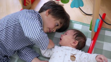 Küçük bir çocuk kareli bir oyun minderinde kardeşiyle sevgi dolu bir şekilde etkileşime girerken sevgi dolu aile ilişkileri ve değerli çocukluk anıları sergiliyor.