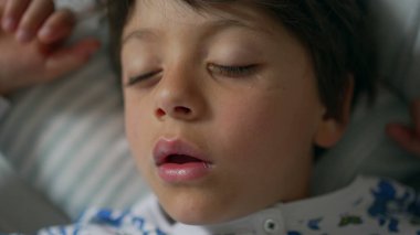 Yakın plan, ağzı açık uyuyan, baskılı pijama giyen, yastıkta huzurlu bir uykuyu ön plana çıkaran bir çocuk.