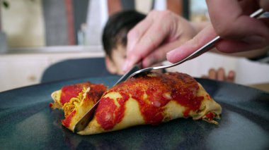 Bir ebeveyn, aile yemeği sırasında yemeğin tadını çıkarmasını kolaylaştırmak için tabakta ev yapımı enchilada kesiyor..