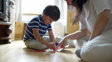 Anne ve oğul yerde eğlenceli ve yaratıcı bir aktivite içinde. Parlak ve neşeli bir ev ortamında odaklanma ve etkileşimle dolu bir anı paylaşıyorlar.