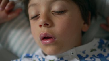 Yakın plan, ağzı açık uyuyan, baskılı pijama giyen, yastıkta huzurlu bir uykuyu ön plana çıkaran bir çocuk.