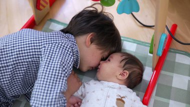 Küçük bir çocuk kareli bir oyun minderinde kardeşiyle sevgi dolu bir şekilde etkileşime girerken sevgi dolu aile ilişkileri ve değerli çocukluk anıları sergiliyor.