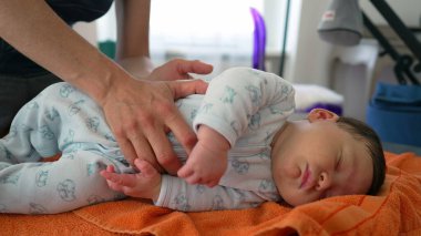 Ortopedist, çocukluk dönemindeki vücut ağrılarını hafifletmek için yeni doğan bebeği turuncu bir havluya nazikçe yerleştiriyor. Bebek bebek tulum giyer. Nazik ve profesyonel bakımı vurgular.