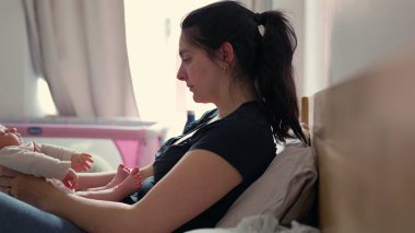 Anne, onu yatağa yatırmadan önce bebeğini öpüyor ve duruşunu düzeltiyor. Sıcak gün ışığı olay yerini aydınlatıyor, samimi bağlarını vurguluyor. Arka planda pembe bebek beşiği