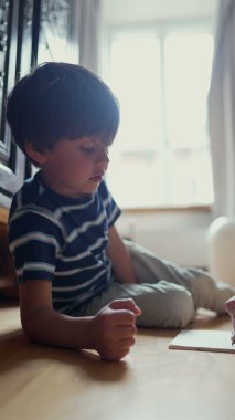 Çocuk yerde odaklanmış bir ifadeyle oturuyor, yardım alarak bir çizim etkinliğine katılıyor, konsantrasyon ve eğitim etkinliği gösteriyor
