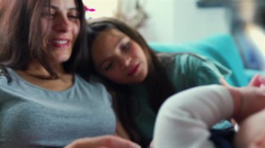 Bir anne ve kızın kanepede otururken, bebeğin eline nazikçe dokunurken, rahatlamış bir aile ortamında bağ kurmaya ve bağ kurmaya odaklanırken.