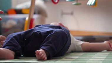 Bir bebeğin oyun hasırına uzanmış, rahat bir ev ortamında oyun sırasında bebek bacakları ve ayaklarını rahat bir pozisyonda gösteriyor.