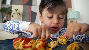 Dağınık saçlı genç bir çocuk ev yapımı enchilada 'lardan büyük bir ısırık alıyor, aile yemeği sırasında keyifle gülümsüyor.