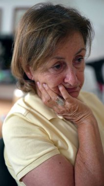 Düşünceli bir yüz ifadesiyle yaşlı bir kadın, yüzünü eline dayamış, bir anlık tefekkür ve sessiz bir yansıma tasvir ediyor.