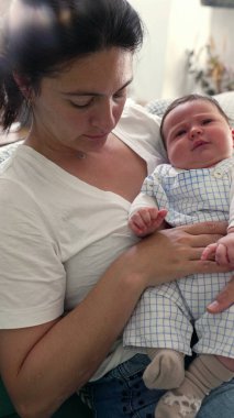 Anne bebeğini kucaklıyor, sıcak bir yuva ortamında sessiz ve sevgi dolu bir anı paylaşıyor, anne ve çocuk arasındaki derin bağı ve sevgiyi vurguluyor.