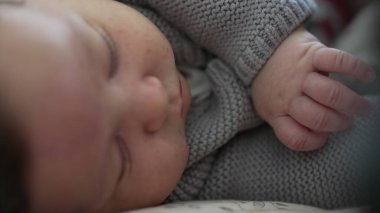 Bir bebeğin huzur içinde uyuduğu, yumuşak bir kazak giydiği, rahat ve güvenli bir ev ortamında sakin ve huzurlu bir anı temsil eden, masumiyetin altını çizen bir fotoğraf.