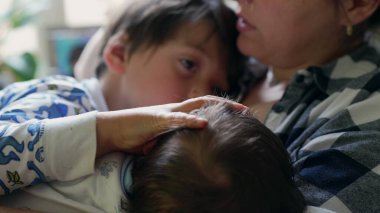 İkisi de annelerinin kucağında uzanırken küçük bir çocuğun nazikçe başını okşaması sevgi ve şefkat dolu samimi bir aile sahnesi yaratıyor.