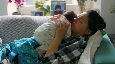 Anne kanepede oturuyor, bebeğini kucağında tutuyor ve onunla nişanlanıyor. Rahat bir ev ortamında anne ve çocuk arasındaki yakın bağ