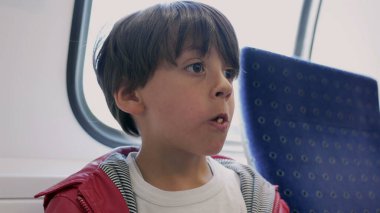 Trende çubuk kraker yiyen genç bir çocuk, yere düşen krakeri yakalayıp, çocukluğunun basit zevkleri olan ağzına geri koyarken merak ve haz gösteriyor.