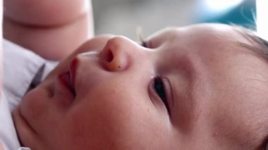 Yatakta dinlenirken kendi elini tutan bir bebeğin yakın çekimi. Yüzün yakınındaki bebek ellerine odaklanın. Yumuşak cildi ve bebek doğal refleksini vurgulayın.