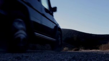 Arka planda güneş parlayan toprak bir yolda giden bir SUV. Off-road macerasını yakalıyor ve engebeli arazide doğa manzaralı bir ortamda yolculuk ediyor.