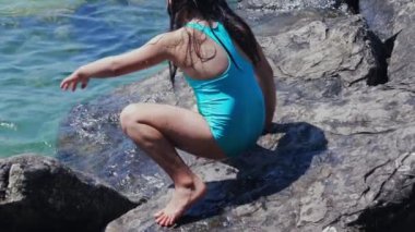 Sahildeki göl kıyısında kayalara tırmanan genç bir kız yüzdükten sonra doğayla ve manzaralı su manzarasıyla çevrili göle atlamaya hazırlanıyor.