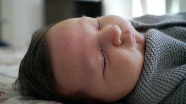 Yeni doğmuş bir bebeğin yüzü, sıcak ve rahat bir ortamda narin özelliklerini ve doğal ifadelerini vurgulayarak uyurken yüzünü buruşturur.
