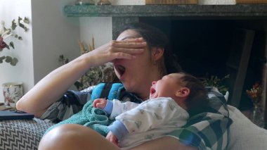 Hem anne hem de bebek kanepede esniyor, sıcak bir ev ortamında senkronize bir yorgunluk ve bağlanma anı, erken ebeveynliğin ortak deneyimlerini yansıtıyor.