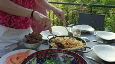 Açık hava yemek masasındaki bir tabağa bir porsiyon makarna servis etmek. Sahnede canlı bir salata, ekmek ve sıcak, ortak bir yemek seti yakalayan bir dizi yemek yer.
