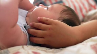 Bebek, büyük bir çocuğun eli bebeğin kafasında yatarken. Yakın plan, evde huzurlu bir ortamda kardeşler arasındaki nazik etkileşimi gösteriyor.
