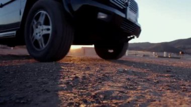 Gün doğumunda kayalık bir toprak yolda arazi aracının tekerleklerini alçak açıyla görmek engebeli arazide gölgeler bırakır. Doğal bir ortamda off-road sürüşünün zorluğu ve macerası