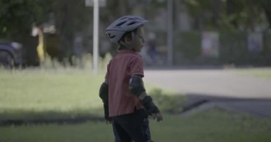 Park yolunda kaykay yapan genç bir çocuk, kask takıyor ve koruyucu giysiler giyiyor, odaklanmış ve kendinden emin bir şekilde ileriye bakıyor, denge ve hareketin özünü yakalıyor.